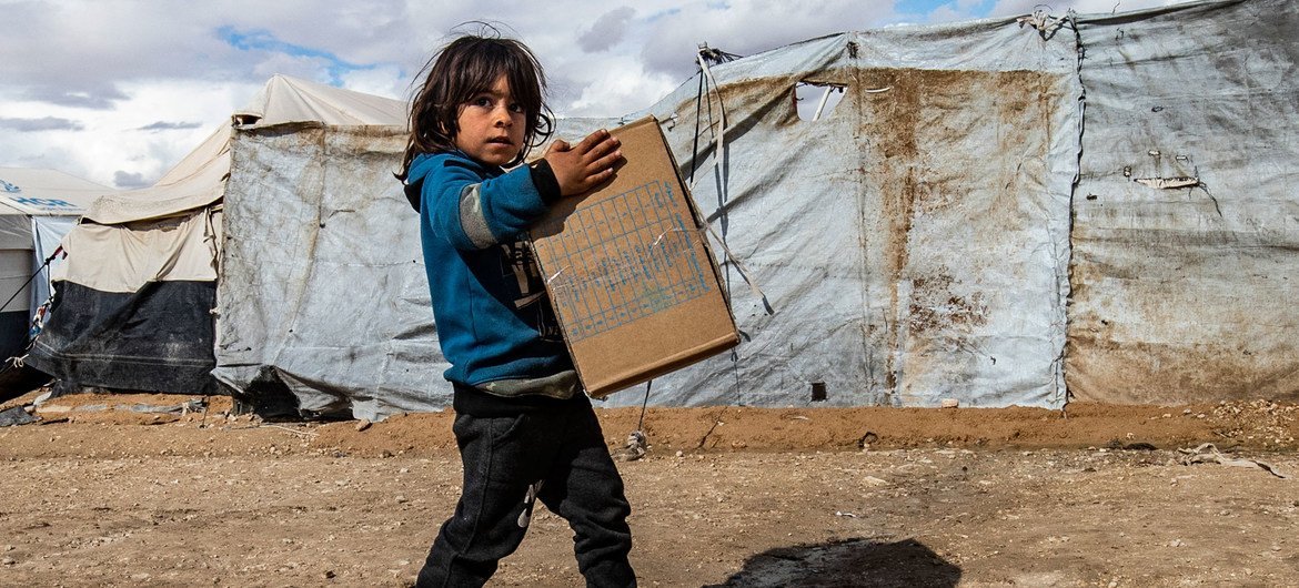 A child carries winter clothing kits, distributed by UNICEF, in Al-Hol camp in northeastern Syria. A child carries winter clothing kits, distributed by UNICEF, in Al-Hol camp in northeastern Syria.