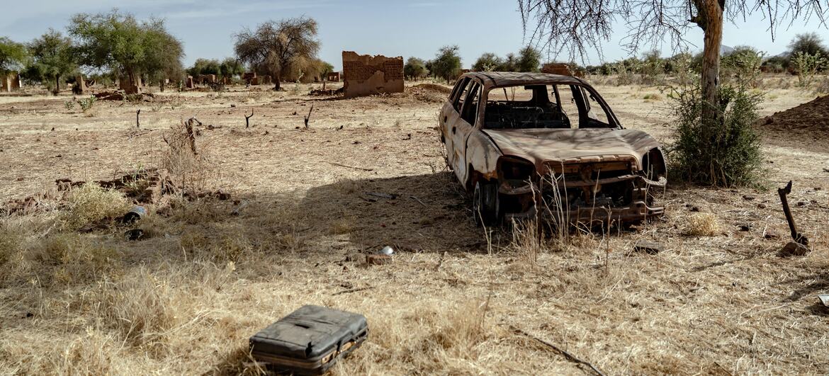 The burnt shell of a car and destroyed mud-brick homes in the abandoned village of Al Bakri in North Darfur, Sudan, showing the aftermath of conflict and displacement.