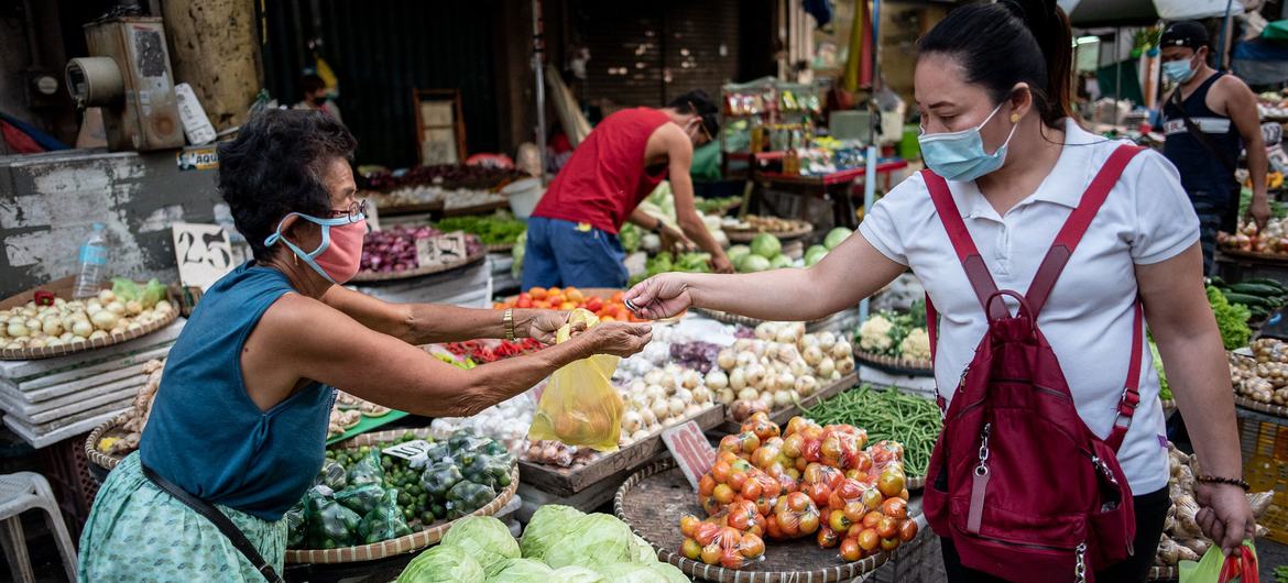 A vegetable vendor serves a customer at a market in Manila, Philippines. A vegetable vendor serves a customer at a market in Manila, Philippines.