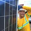 A Filipino construction worker in a yellow safety shirt and white hard hat smiles while leaning against a large solar panel during the UNDP Renewable Energy project in BARMM, Philippines.