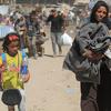 Displaced Palestinian women and children walk through a dusty street carrying belongings, photographed during a press conference in Cairo in April 2025.