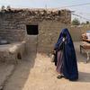 A woman in a blue burqa stands in the courtyard of a mud-brick house in Surkh Rod, Jalalabad, Afghanistan. The community received winter relief items.