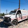 A severely damaged white ambulance with shattered windows and bullet holes sits amidst rubble on a street in Tebnine, Lebanon, showing the impact of conflict on emergency services.