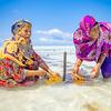 Two rural women in Tanzania harvest seaweed in shallow coastal water.