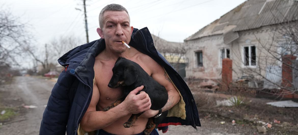 A man holds a dog as he walks past a damaged house following shelling in Mariupol, in southeastern Ukraine. A man holds a dog as he walks past a damaged house following shelling in Mariupol, in southeastern Ukraine.