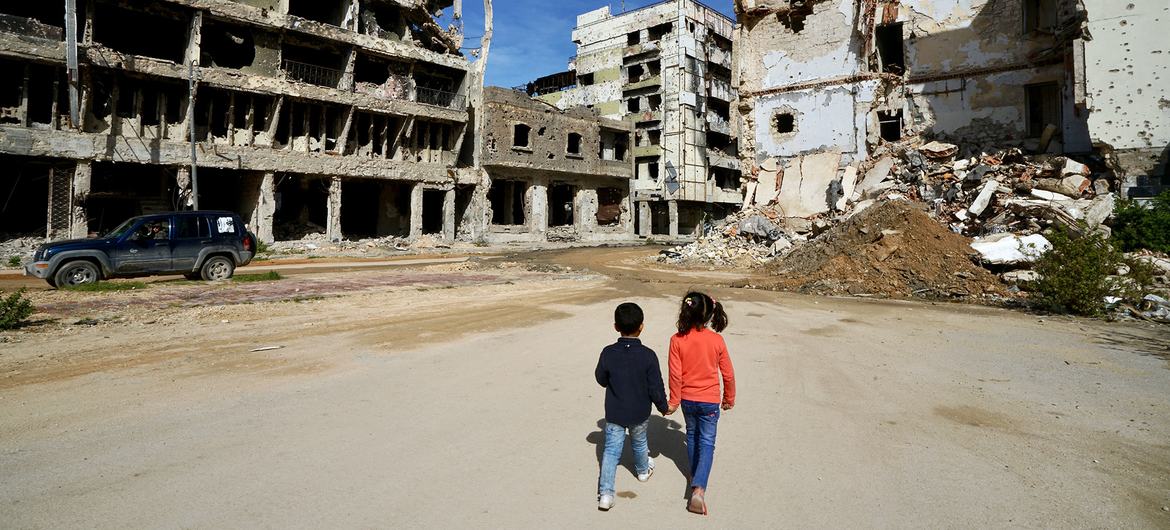 Libya'da Bingazi'de çocuklar hasarlı binaların yanından geçiyor.