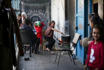 A Palestinian girl cooks in a courtyard of a UNRWA school in the Deir al-Balah refugee camp in Gaza, while other displaced children and women look on.