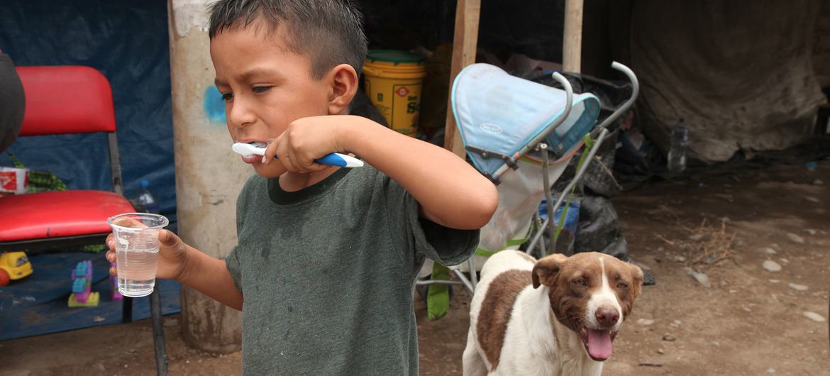 Evi sel nedeniyle yıkılan yerinden edilmiş bir çocuk, Peru, Lima'daki geçici bir barınağın önünde dişlerini fırçalıyor.