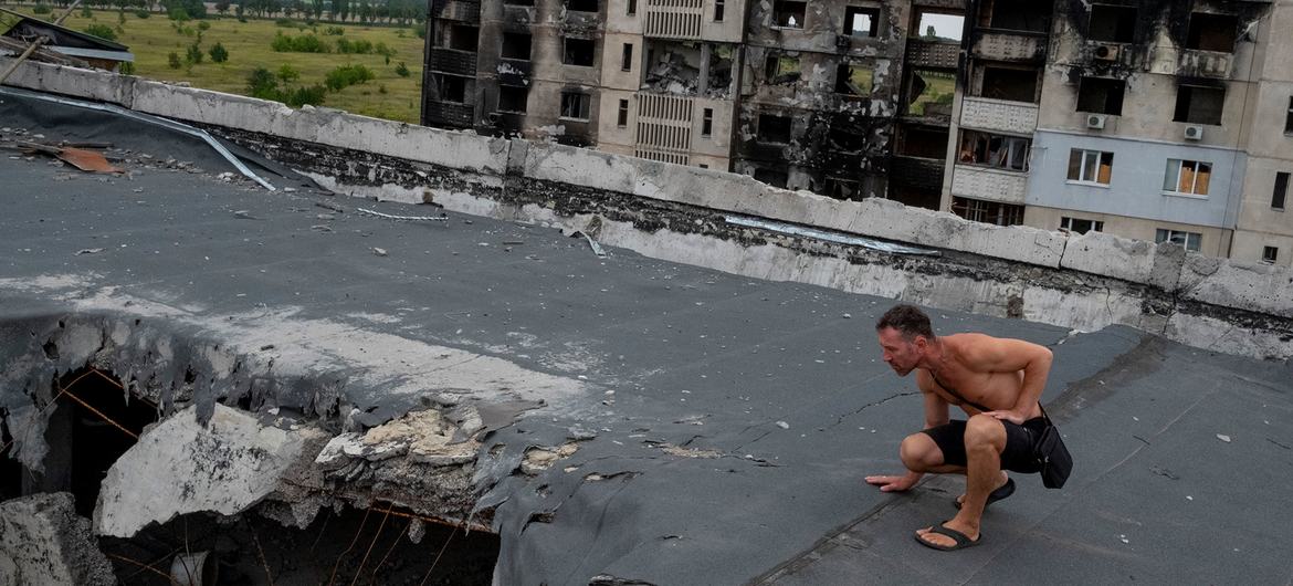 Bir adam, Kharkiv banliyösünde topçu ve hava saldırılarıyla yıkılan bir apartman kompleksinin çatısındaki hasarı inceliyor.