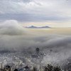 A view of the city of Tehran, Iran, from Velenjak, with thick fog and clouds obscuring the lower buildings and distant mountains.