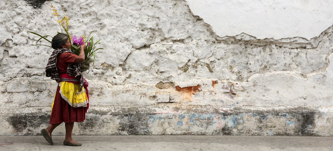 A woman carries a basket of flowers next to the cobblestone streets and crumbling walls of Antigua, Guatemala.