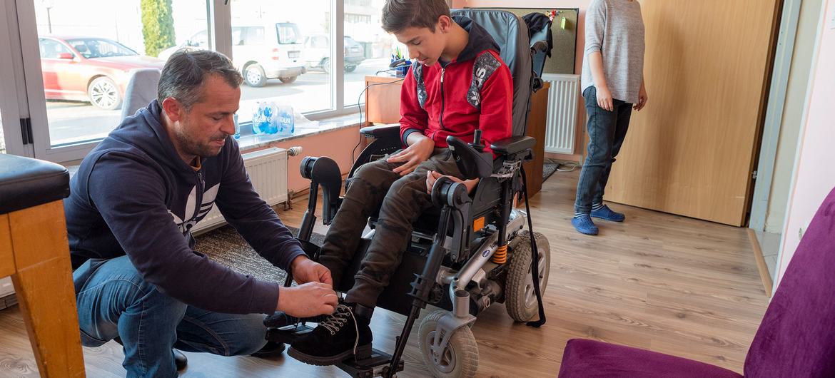 In Kosovo, a father helps his son, who suffers from cerebral palsy, get back into his electric wheelchair. In Kosovo, a father helps his son, who suffers from cerebral palsy, get back into his electric wheelchair.