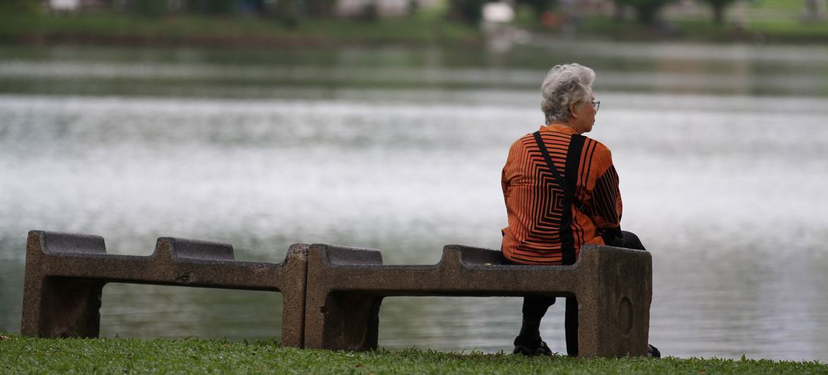 An elderly woman sits alone on a bench near a pond in Thailand. An elderly woman sits alone on a bench near a pond in Thailand.