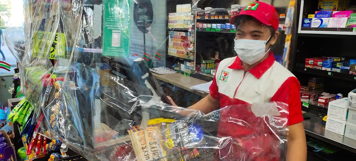 A convenience store requires staff to wear a mask, observe physical distance, and use a plastic sheet barrier as safety measures to prevent the spread of COVID-19, Muntinlupa City, Philippines.