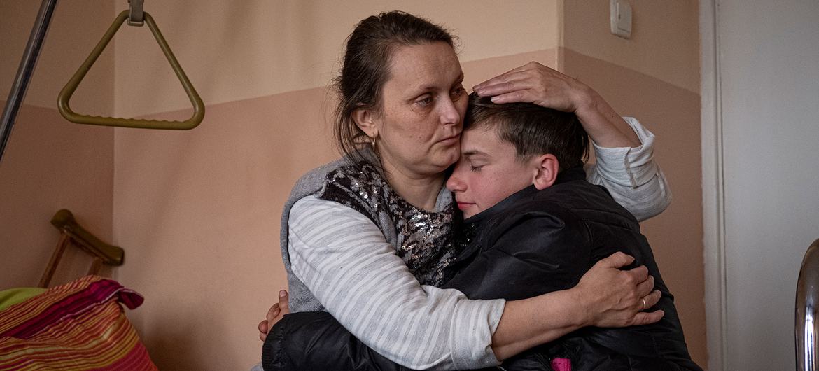 On iki yaşında bir erkek çocuk, bir ay önce şarapnel ile yaralanmasından bu yana annesini ilk kez hastanede ziyaret ediyor.