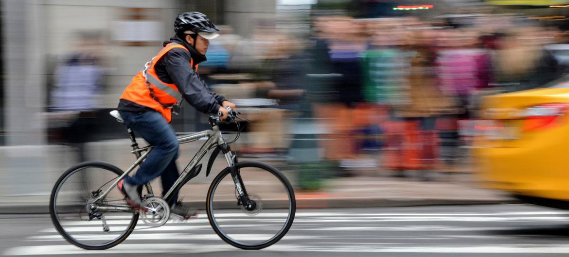 Bir adam Manhattan, New York'ta bisiklet sürerken kask ve yansıtıcı yelek giyiyor.