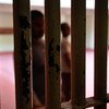 Two blurred figures stand behind the vertical bars of a prison cell in Malé, Maldives.
