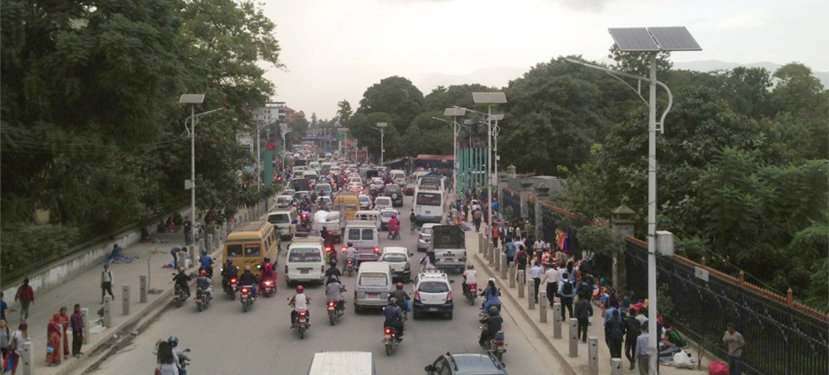 A high-angle view of a busy, congested street in Kathmandu, Nepal, filled with a mix of cars, buses, motorcycles, and pedestrians.